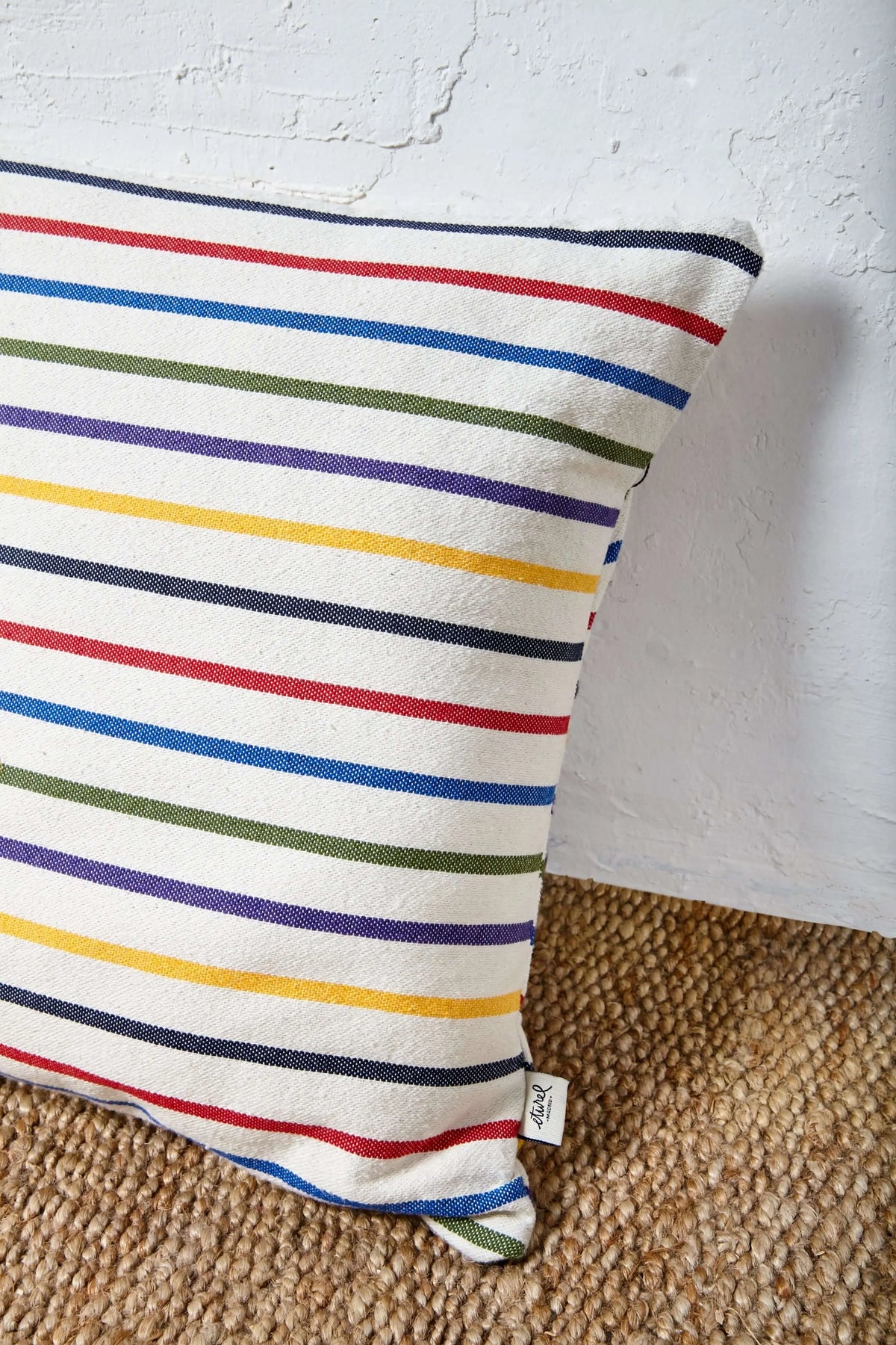 Funda de cojín de 50x50 cm, tejido de algodón con rayas horizontales multicolores sobre fondo crudo, estilo artesanal.