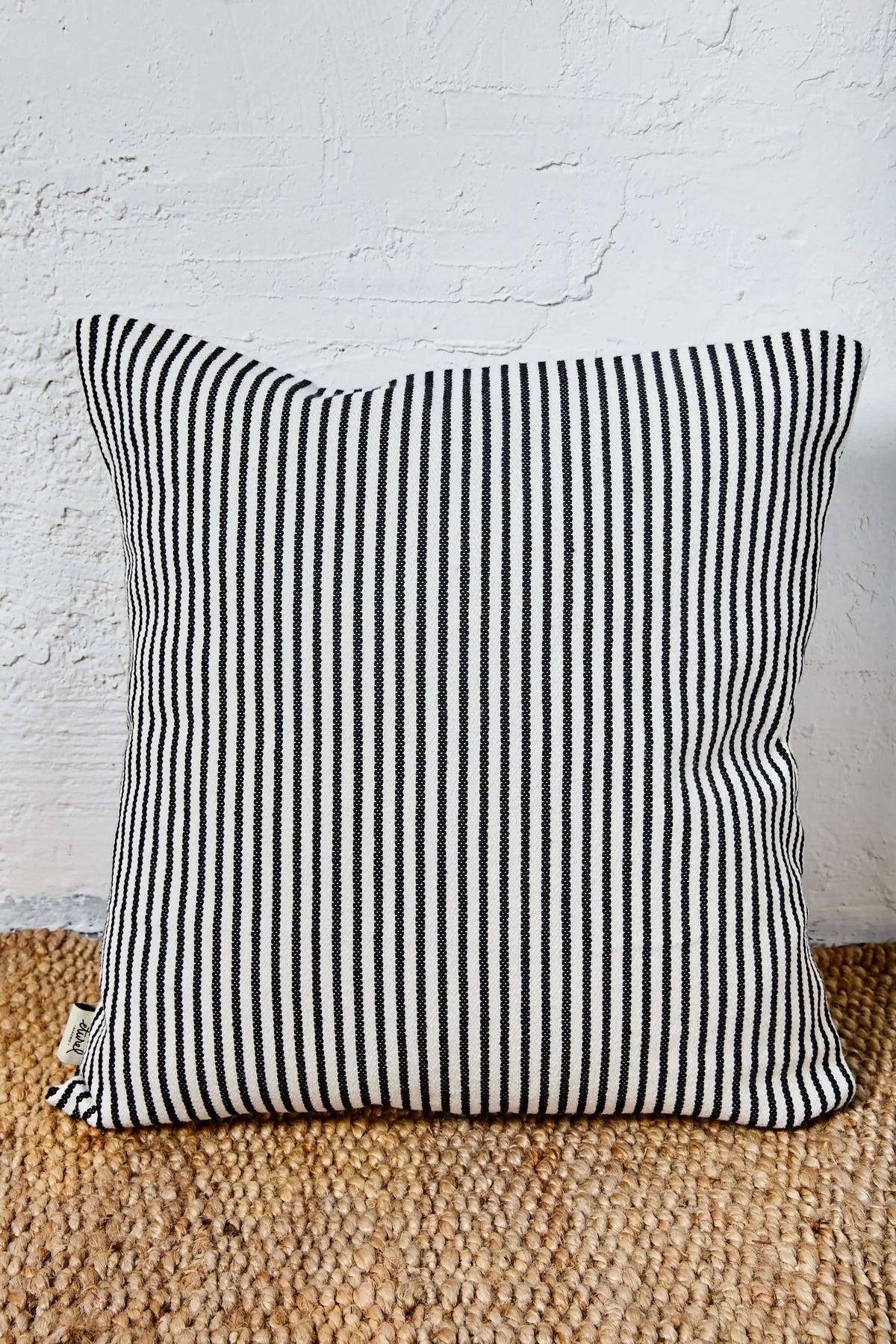 Funda de cojín cuadrada de 50x50 cm en loneta con estampado de rayas verticales finas en blanco y negro.