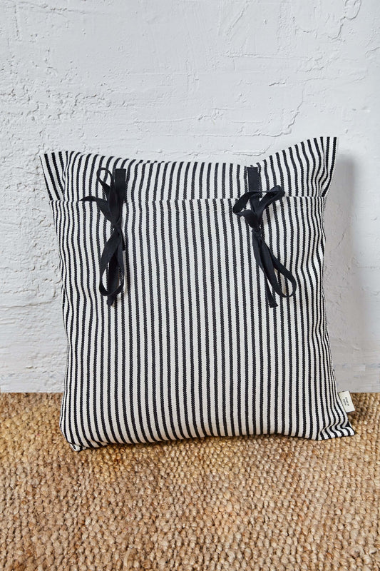 Funda de cojín de loneta a rayas blancas y negras, cuadrada, con dos lazos decorativos negros y cierre tipo estribera.