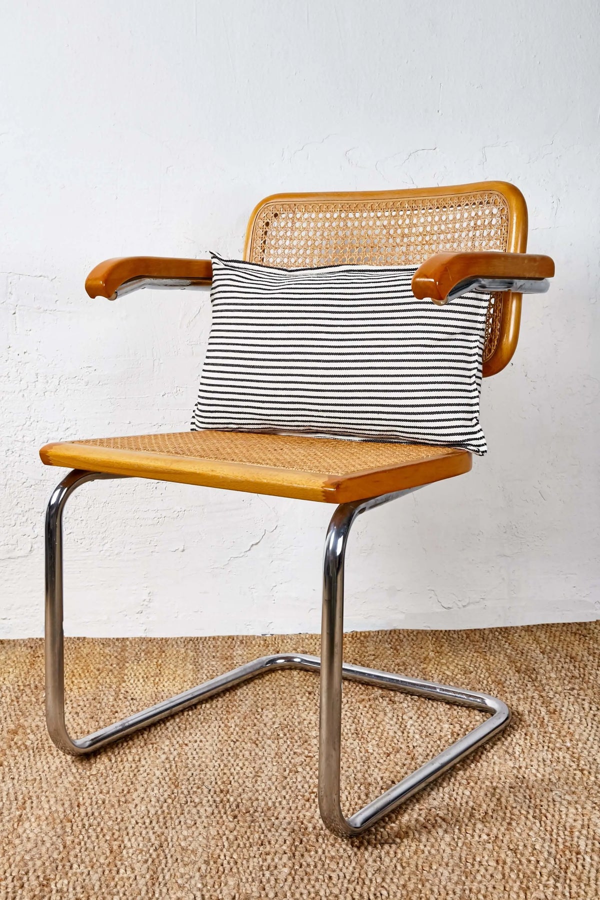 Cojín rectangular de loneta a rayas horizontales blanco y negro sobre una silla de madera y metal estilo retro.