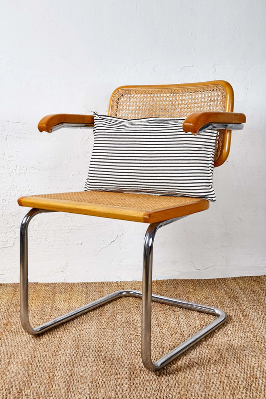 Cojín rectangular de loneta a rayas horizontales blanco y negro sobre una silla de madera y metal estilo retro.