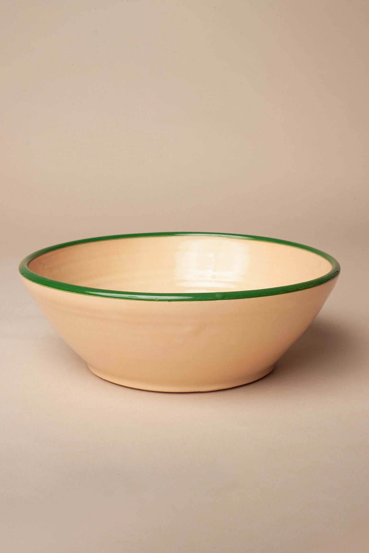 A round, beige ceramic salad bowl with a smooth finish and a contrasting dark green painted rim.
