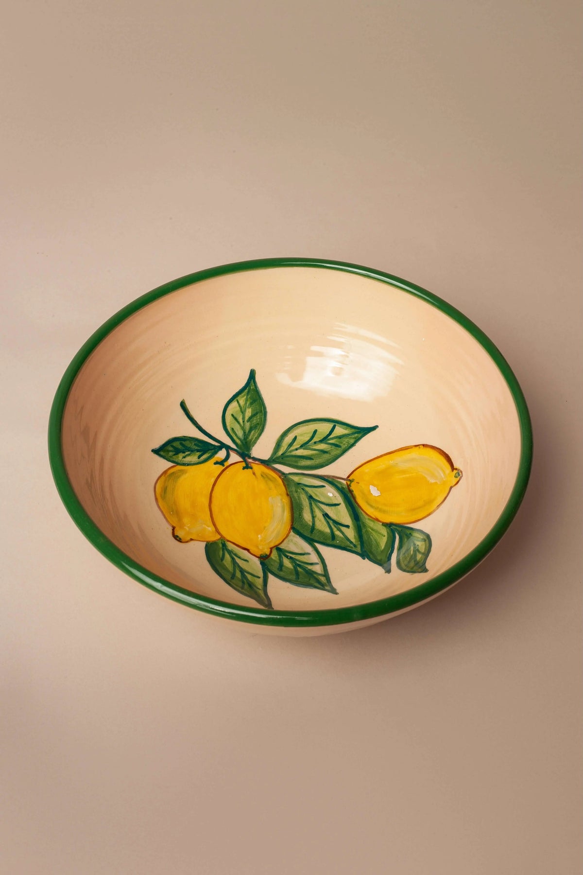 Ensaladera de cerámica color crema con borde verde y estampado artesanal de limones amarillos con hojas verdes.
