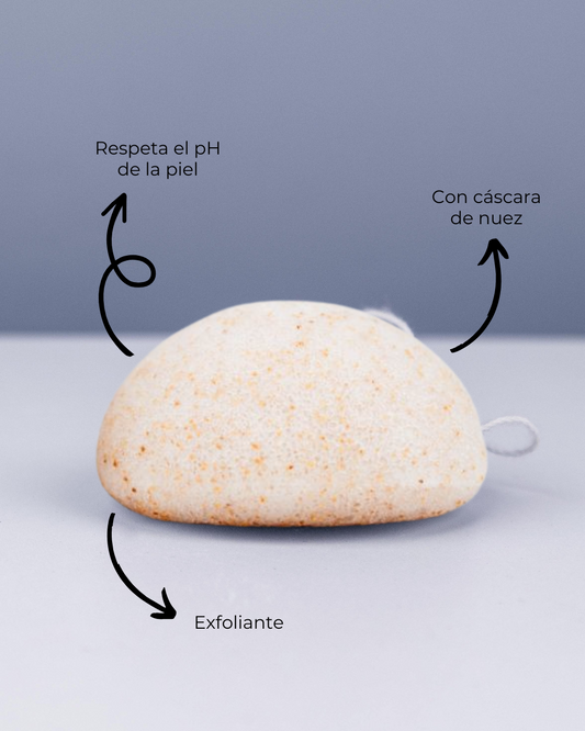 Esponja Konjac exfoliante Banbu de color crema con partículas de nuez sobre fondo gris, con etiquetas explicativas.