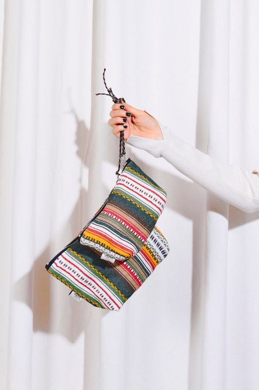 Neceser de tela con estampado alpujarreño de rayas coloridas, textura tejida y cremallera, sostenido por una mano.