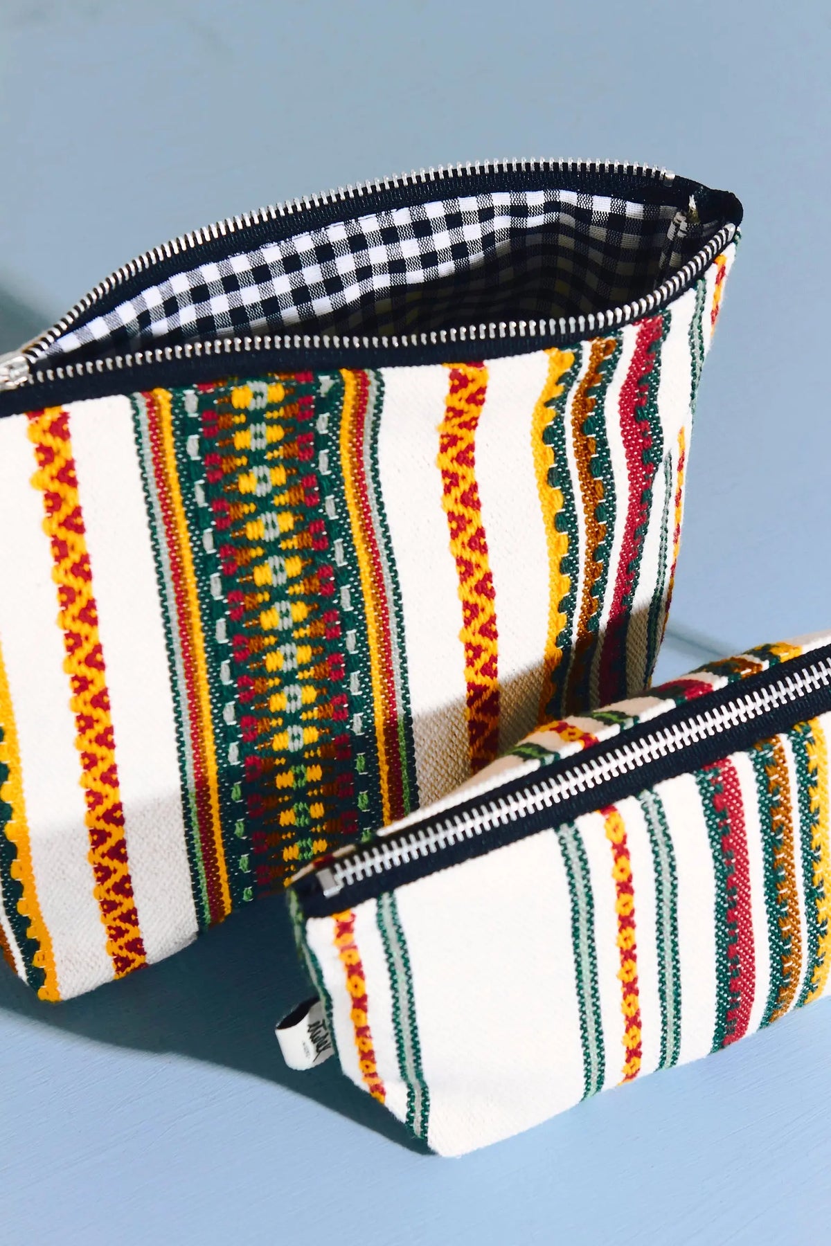 Neceser y estuche de tela cruda con rayas verticales de colores rojo, verde y amarillo, con cremallera y forro de cuadros.