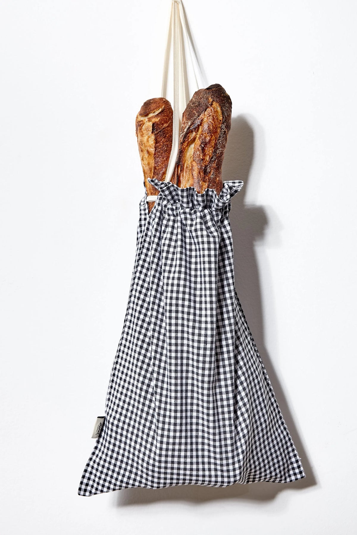 Panera de tela con estampado de cuadros vichy en blanco y negro, colgando con barras de pan en su interior.