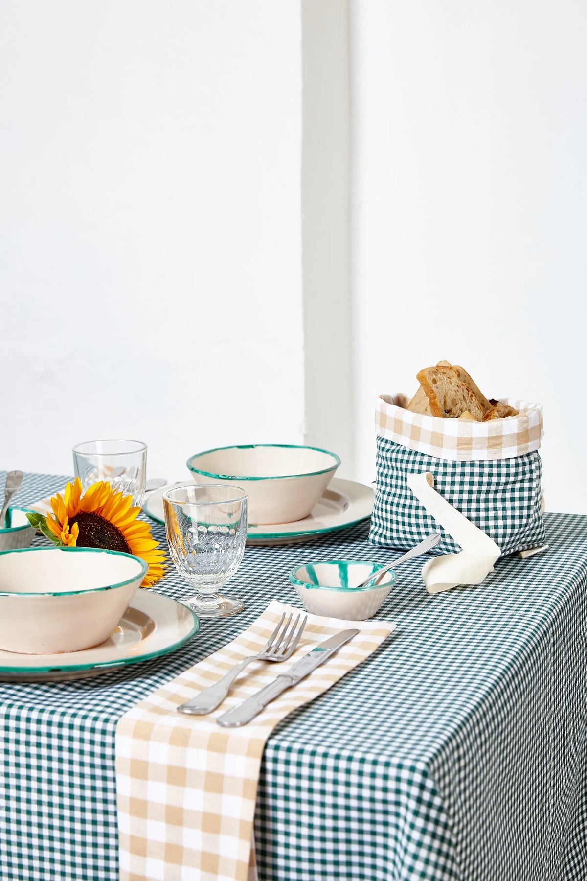 Mantel de algodón con estampado de cuadros vichy verde botella sobre una mesa puesta con vajilla artesanal.
