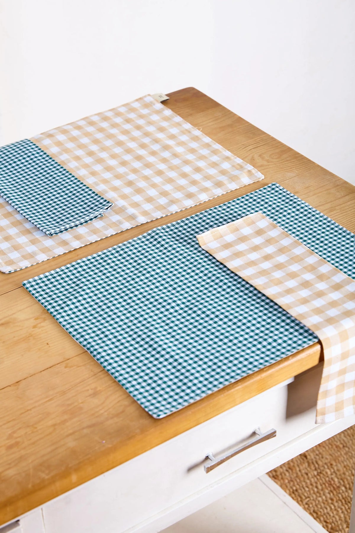 Set de dos servilletas de tela con estampado de cuadros vichy en verde y beige sobre una mesa de madera.