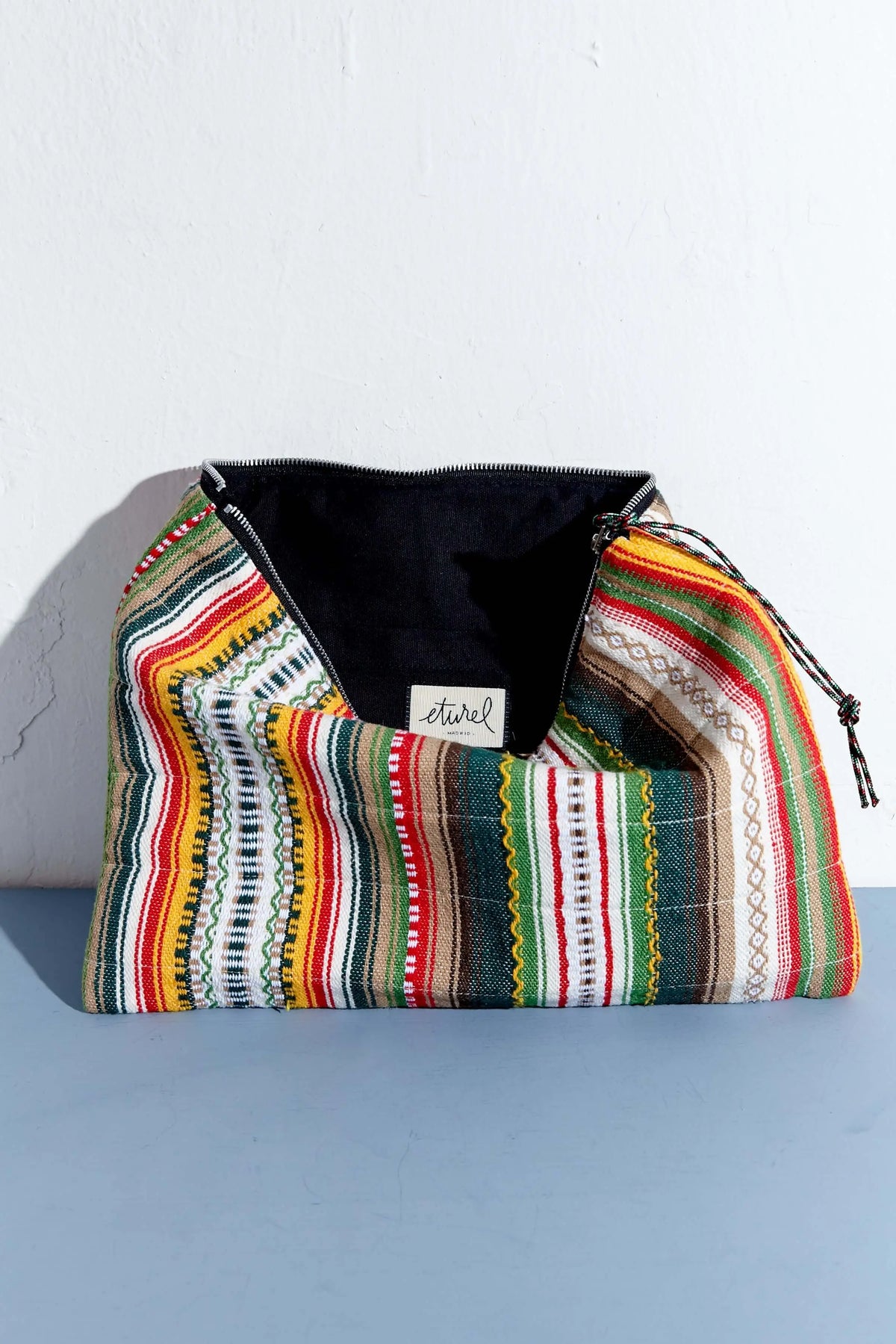 Laptop sleeve with colorful, multi-striped woven fabric, black interior lining, and a top zipper closure.