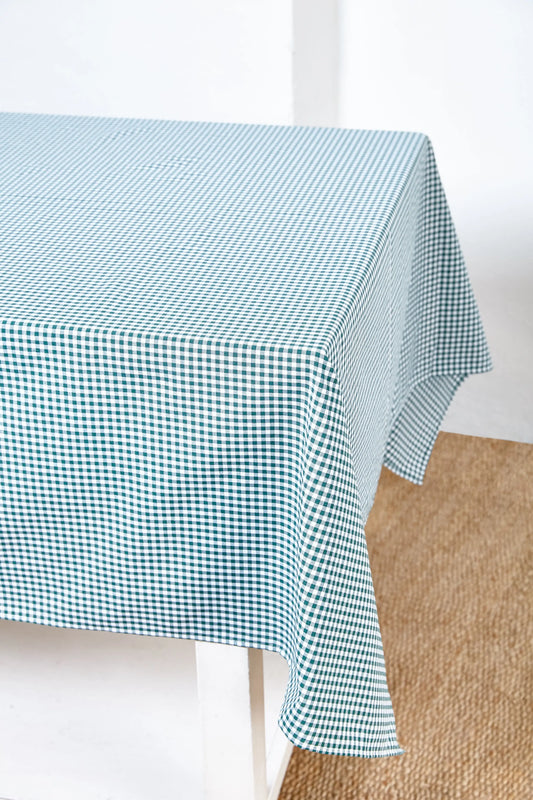Mantel de tela con estampado de cuadros vichy en color verde botella sobre una mesa blanca.