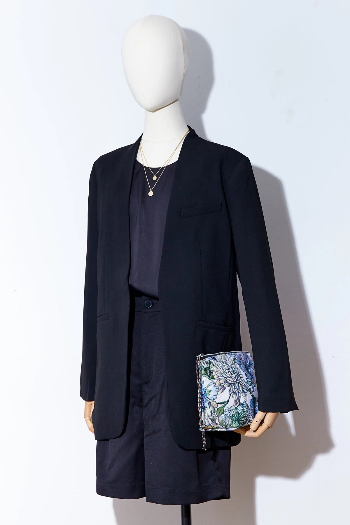 Neceser tipo estuche con estampado de flores y crisantemos azules en tejido jacquard sobre maniquí con traje negro.