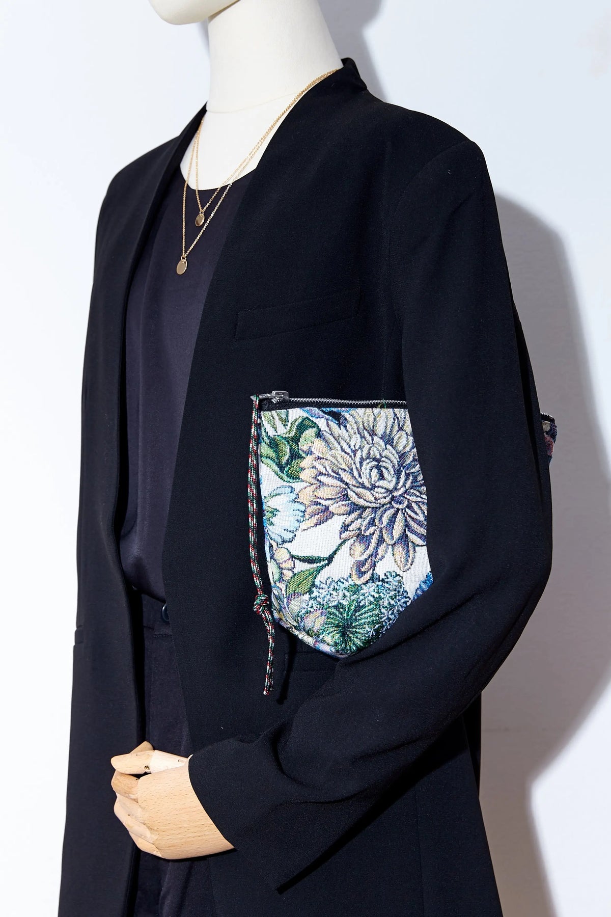 Neceser de tejido jacquard con estampado de crisantemos azules sostenido por un maniquí con chaqueta negra.