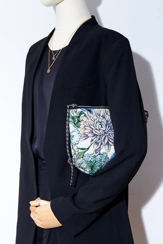 Neceser de tejido jacquard con estampado de crisantemos azules sostenido por un maniquí con chaqueta negra.