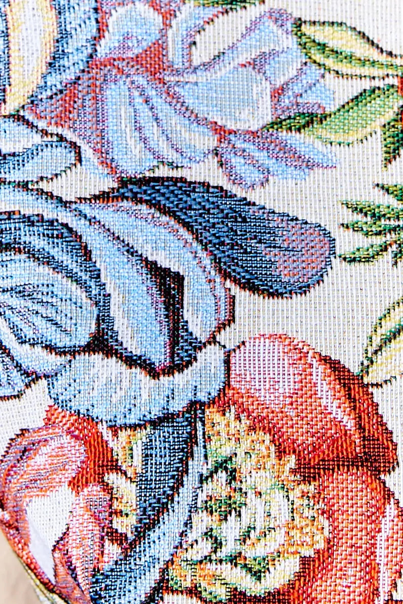 Primer plano de tejido jacquard con estampado floral de crisantemos rojos, azules y verdes sobre fondo blanco.