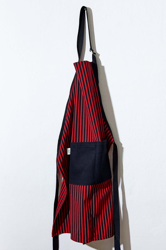 Delantal de loneta ajustable con estampado de rayas verticales rojas y negras, con bolsillo frontal negro.