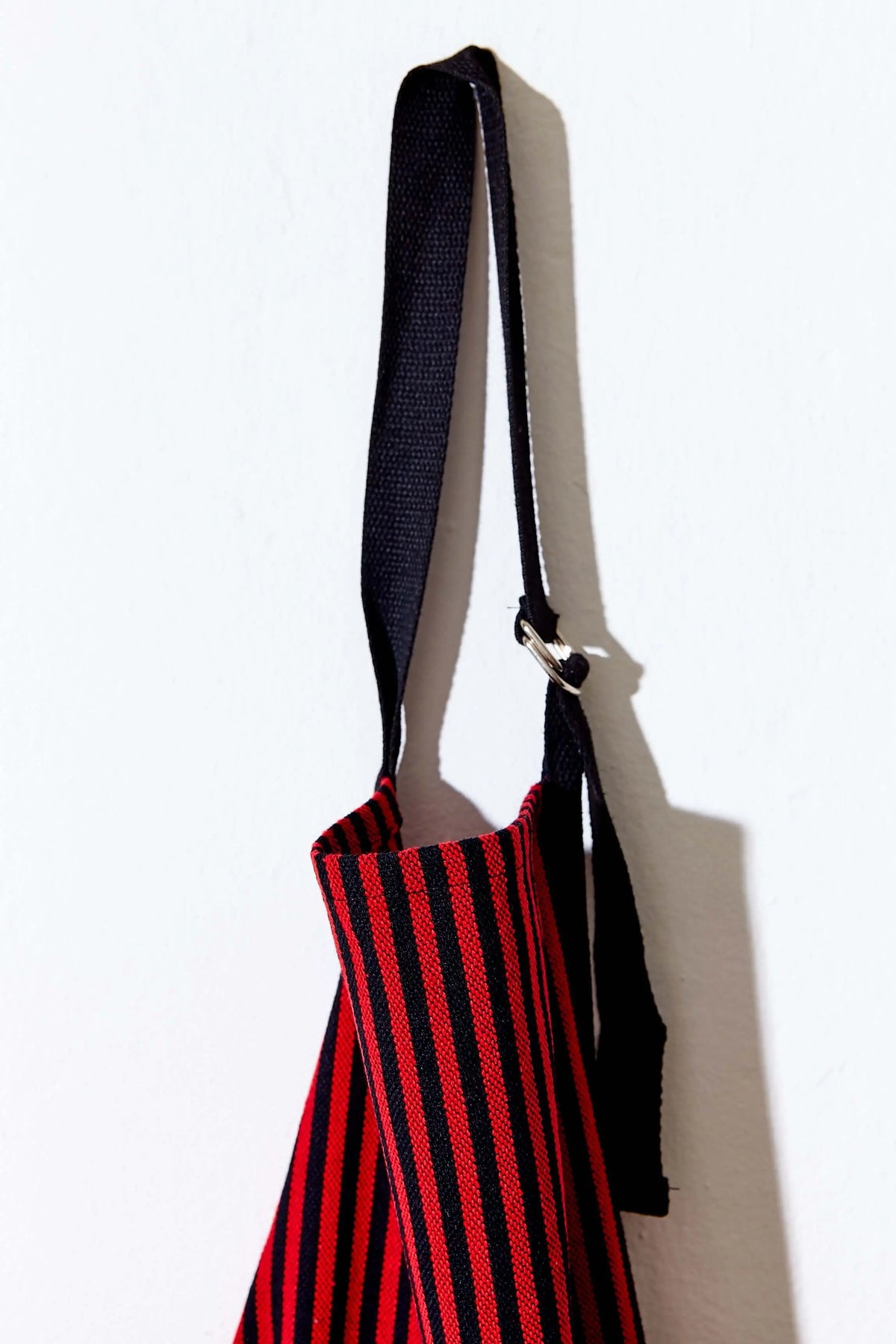 Delantal de loneta con rayas rojas y negras, estilo estribera, con cinta ajustable negra y hebilla metálica.