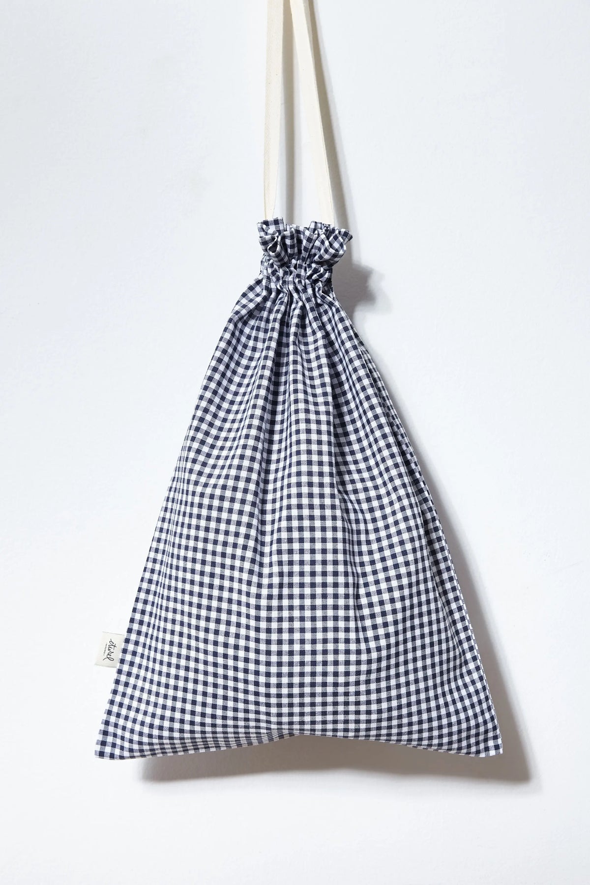 Panera de tela con estampado de cuadros vichy azul marino y blanco, forma alargada y cierre de cordón ajustable.