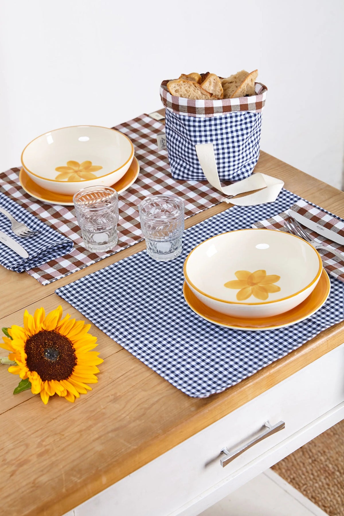 Dos servilletas de tela con estampado de cuadros vichy azul marino, dispuestas sobre una mesa con vajilla.