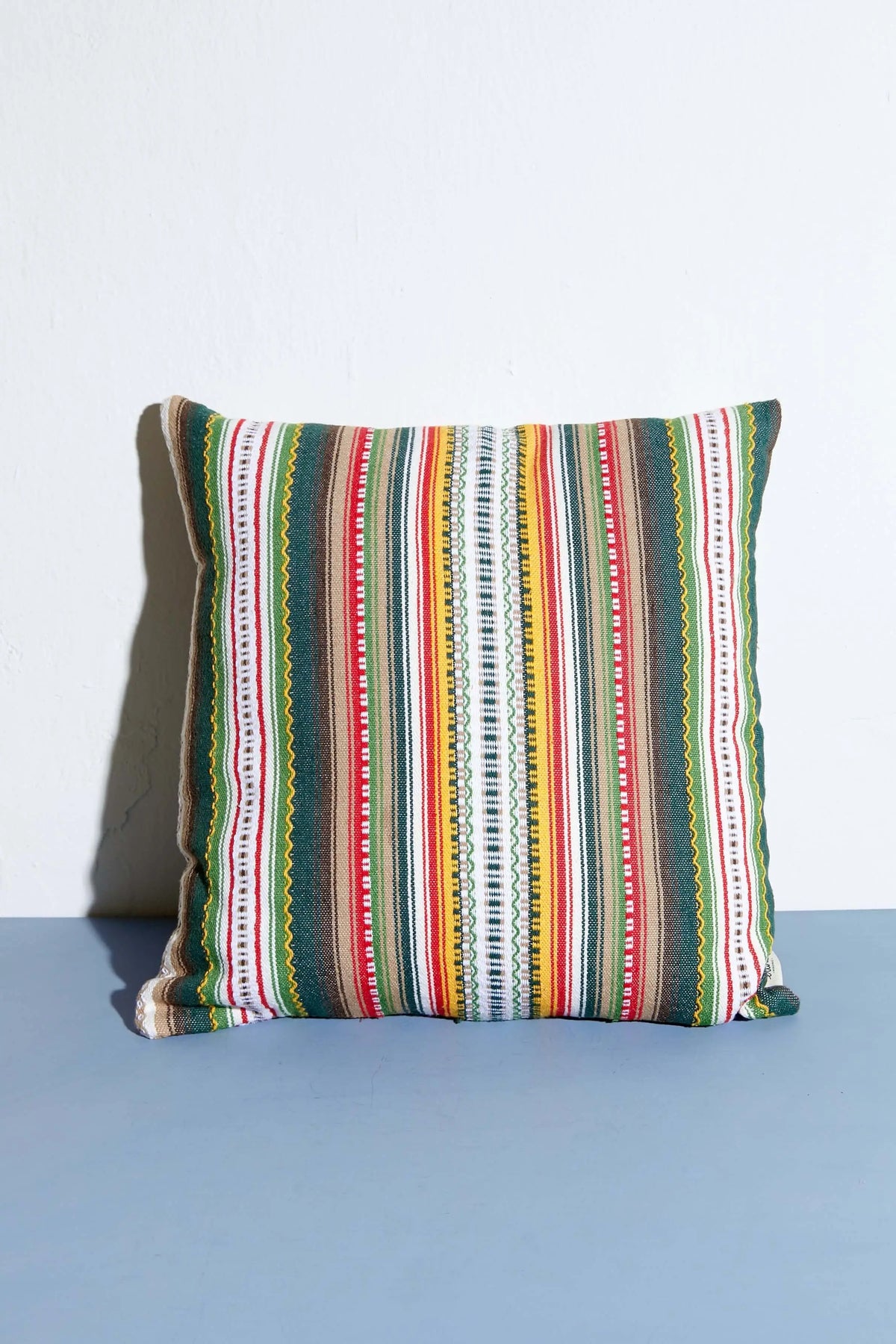 Cojín cuadrado de 50x50 cm con estampado de rayas verticales multicolores y texturas estilo artesanal alpujarreño.