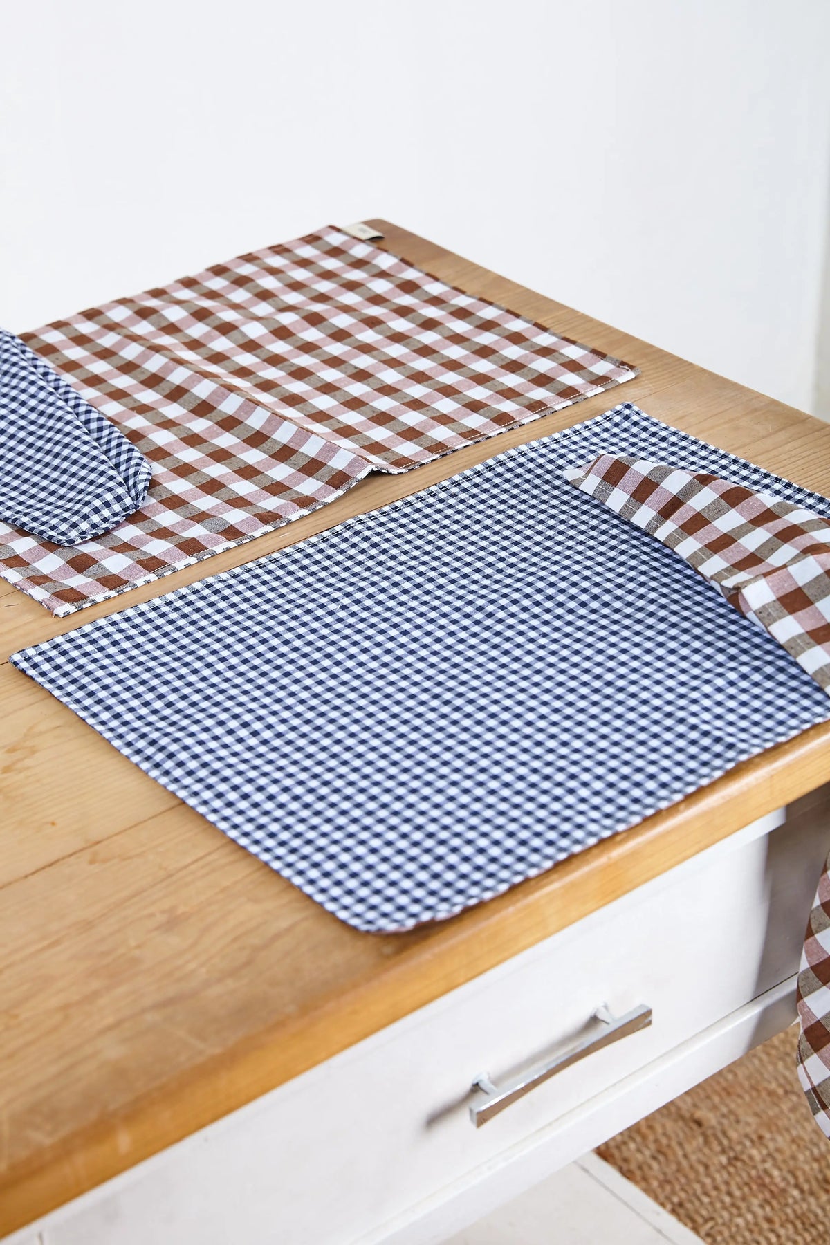 Dos servilletas rectangulares de tela con estampado de cuadros vichy, una en azul marino y otra en tono marrón.