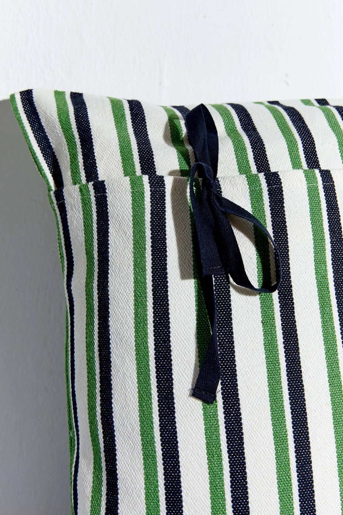 Funda de cojín de loneta con rayas verticales verdes, negras y blancas, con cierre de lazo negro lateral. 50x50 cm.
