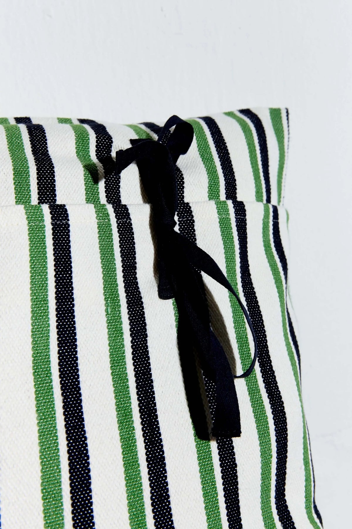 Funda de cojín de loneta con rayas verticales verdes y negras, acabado en lazo negro sobre fondo blanco. 50x50 cm.