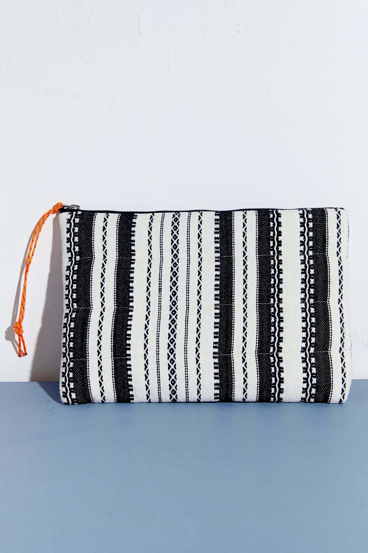 Funda para ordenador o tablet de estilo alpujarra con estampado de rayas verticales en blanco y negro y tirador naranja.