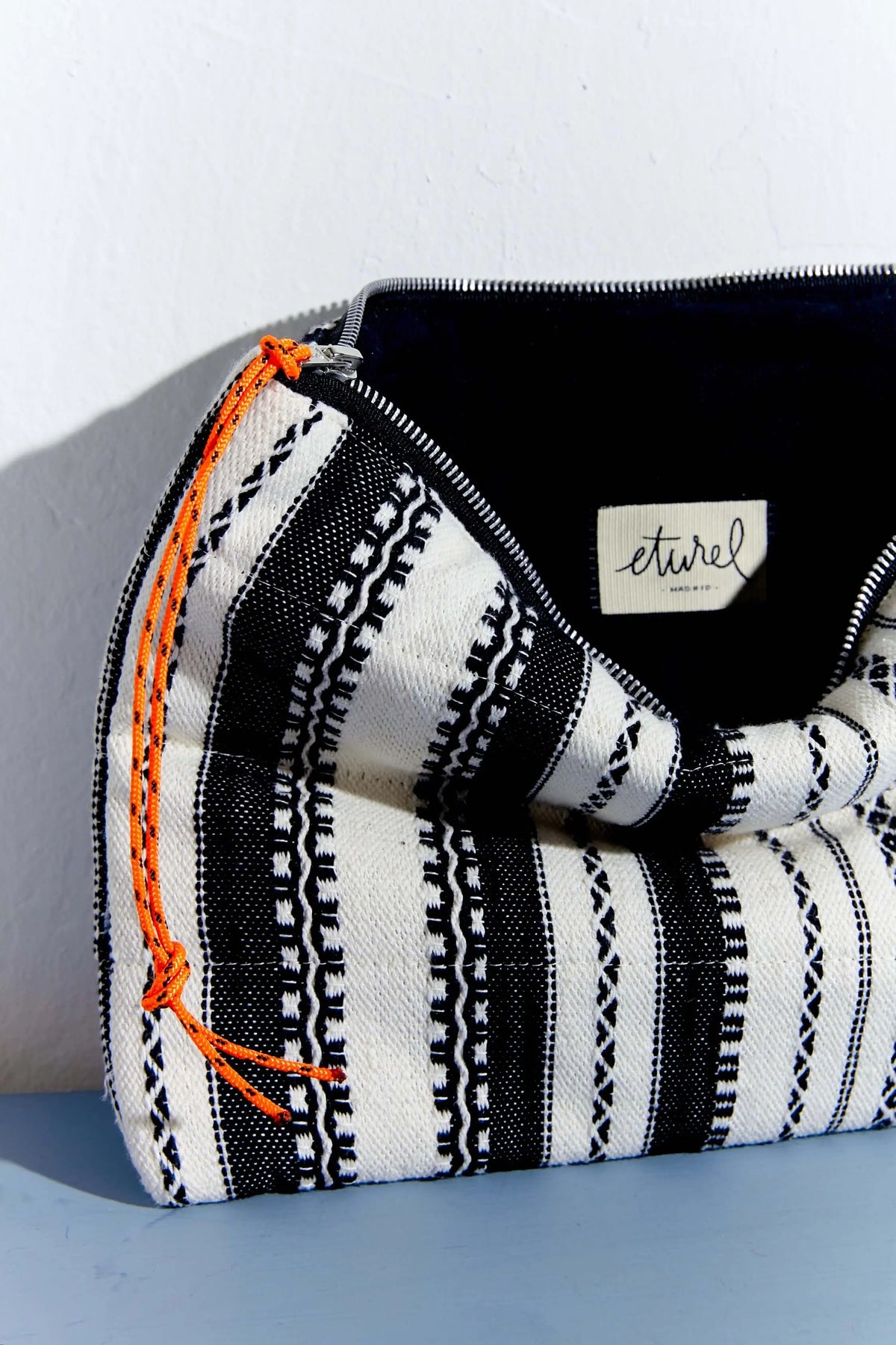 Funda para ordenador con tejido textil de rayas blancas y negras, cremallera con detalle de cordón naranja.
