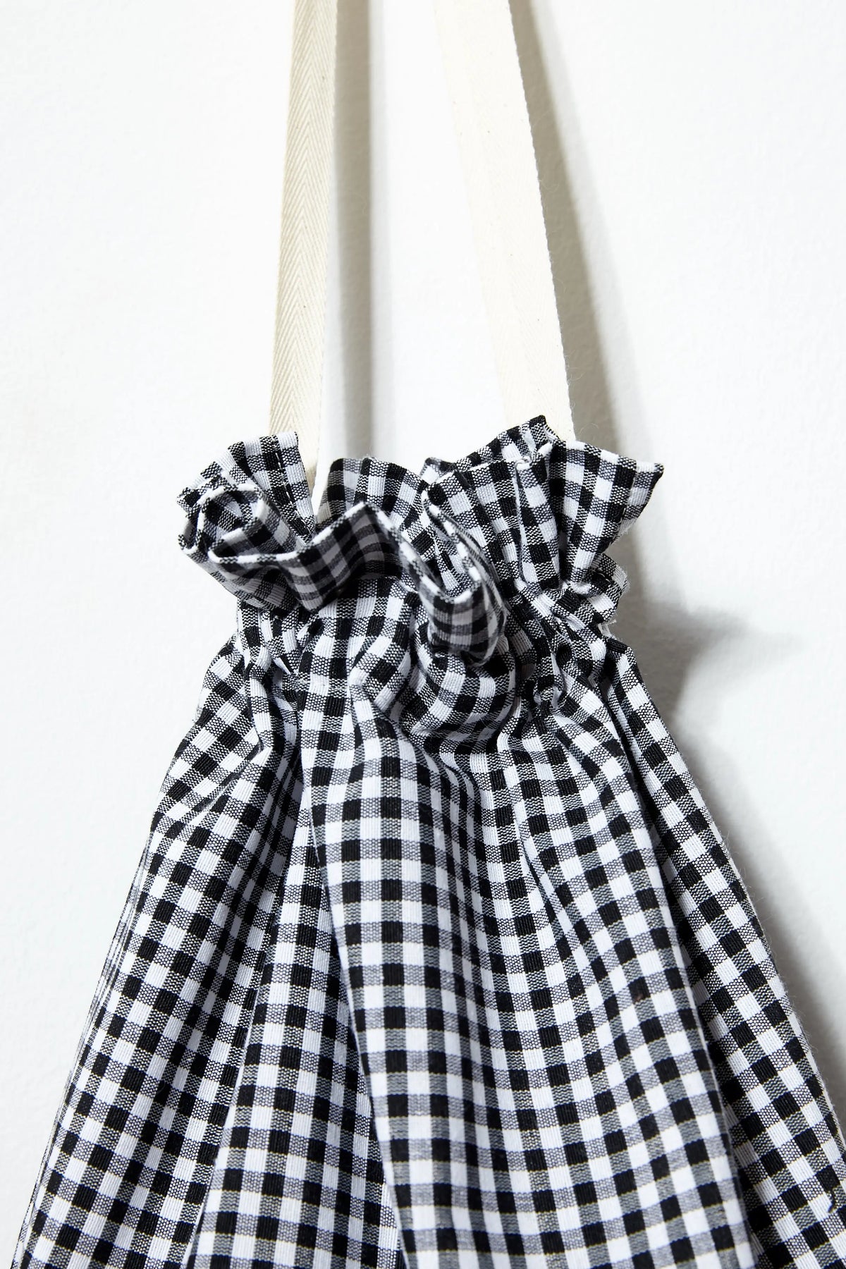 Black and white gingham fabric bread bag with a gathered drawstring top and off-white cotton ribbon handles.
