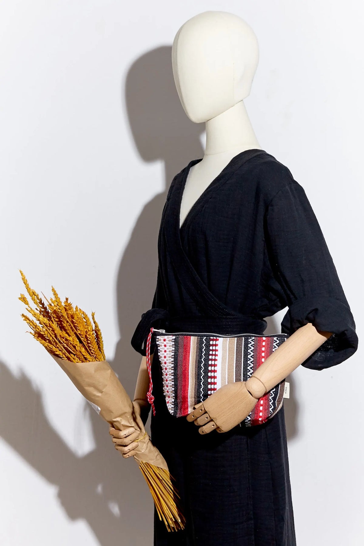 Neceser de tela con tejido manchego a rayas rojas, negras y blancas, con cierre de cremallera y tirador decorativo.