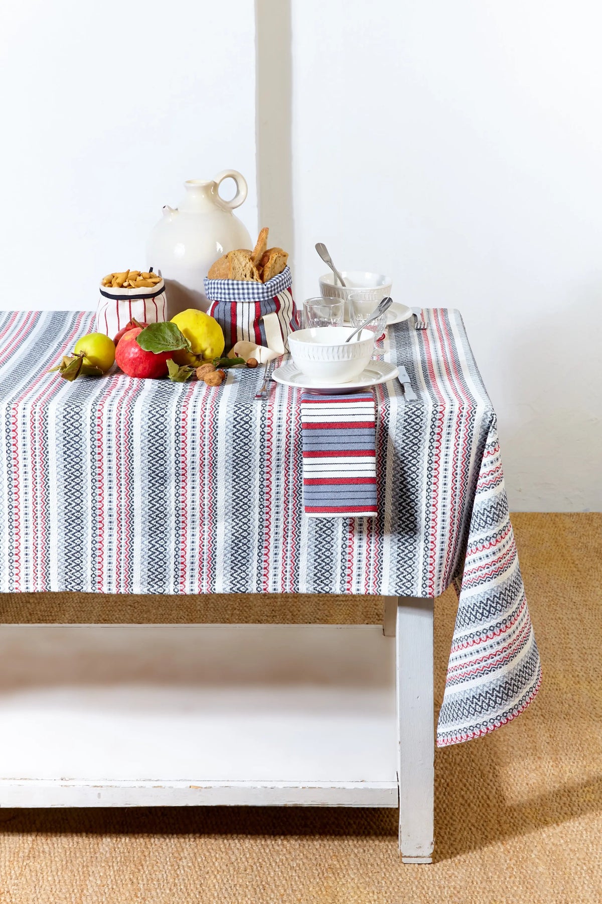 Mantel de tejido rústico con estampado de rayas verticales en tonos granate, gris y blanco sobre mesa decorada.