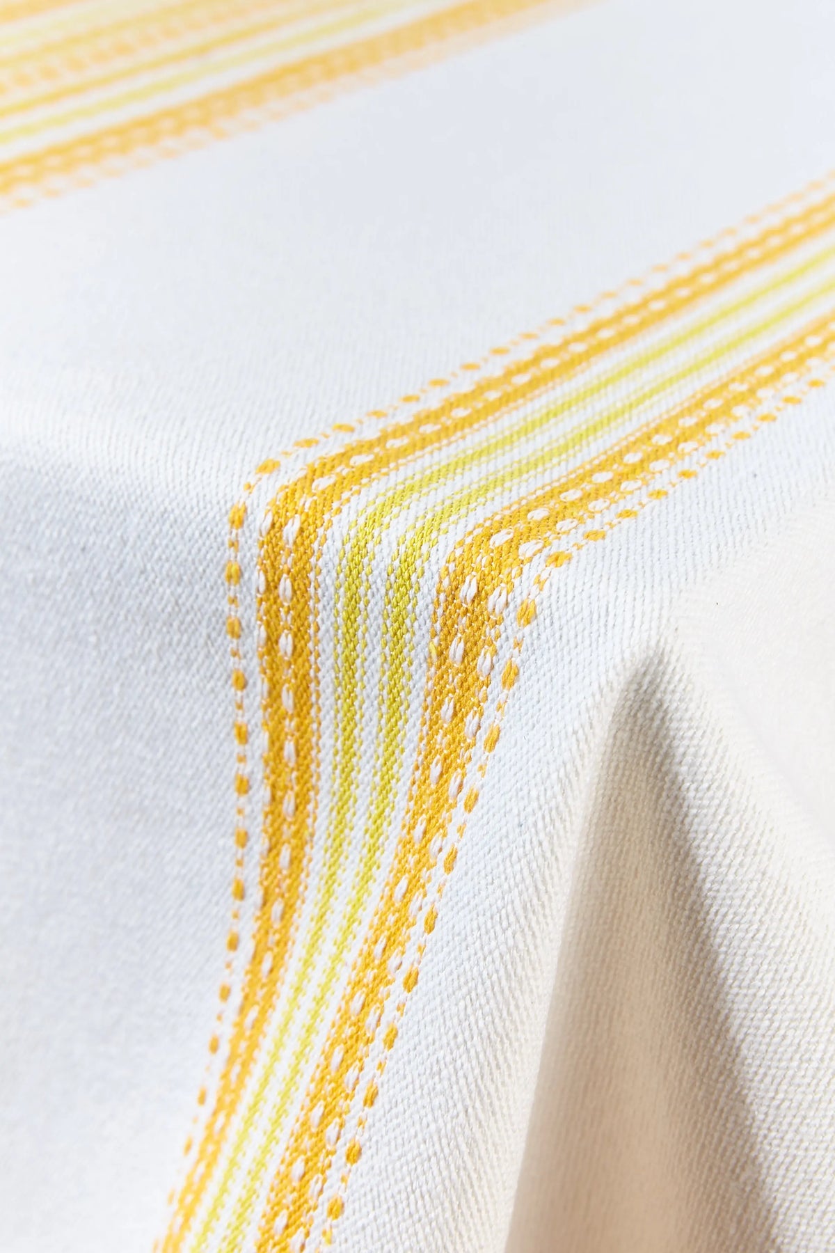 Mantel de tela blanca con rayas verticales texturizadas en tonos amarillos, estilo alpujarreño de tejido resistente.