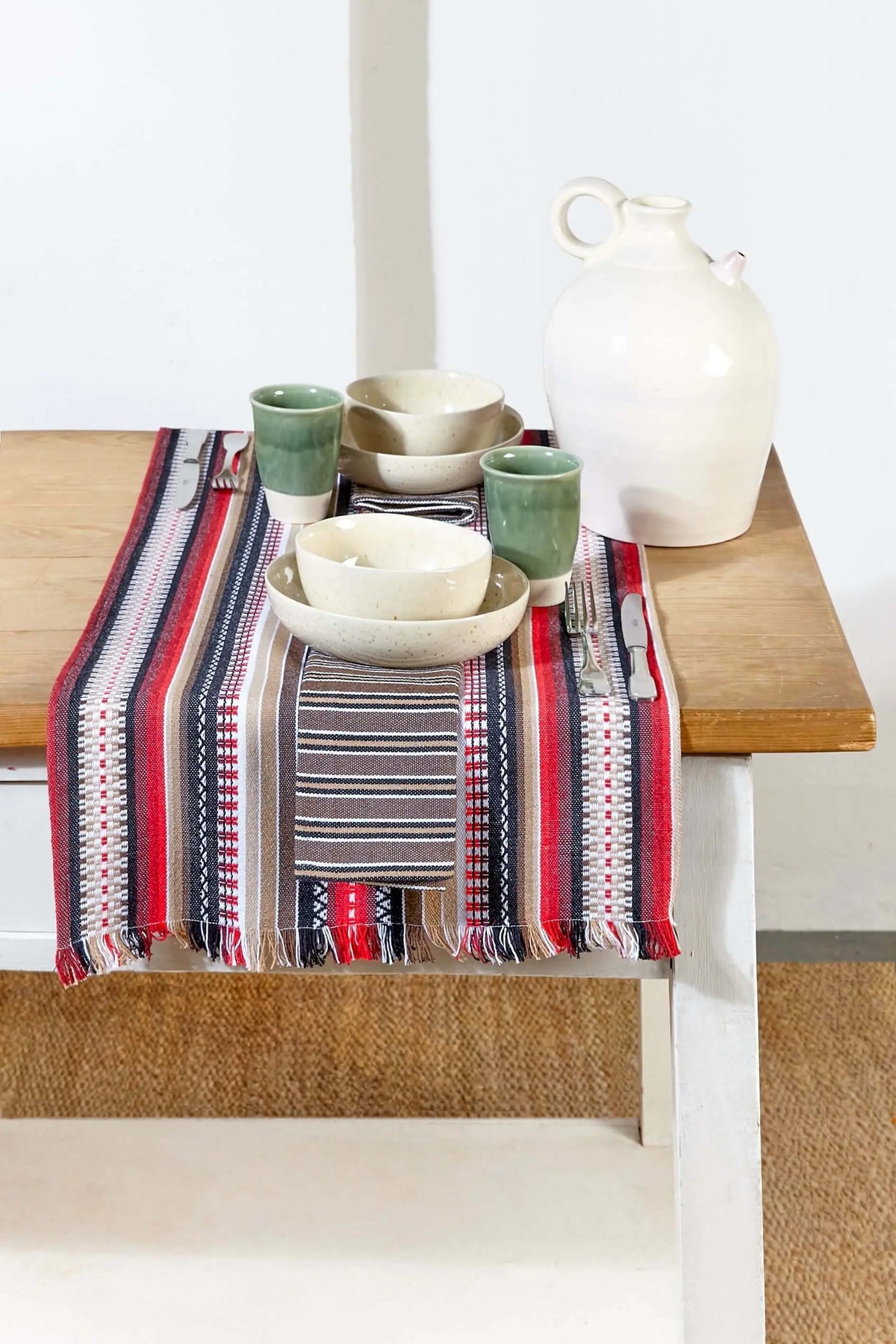 Red woven table runner featuring traditional stripes, patterns, and fringe edges, displayed on a wooden table.