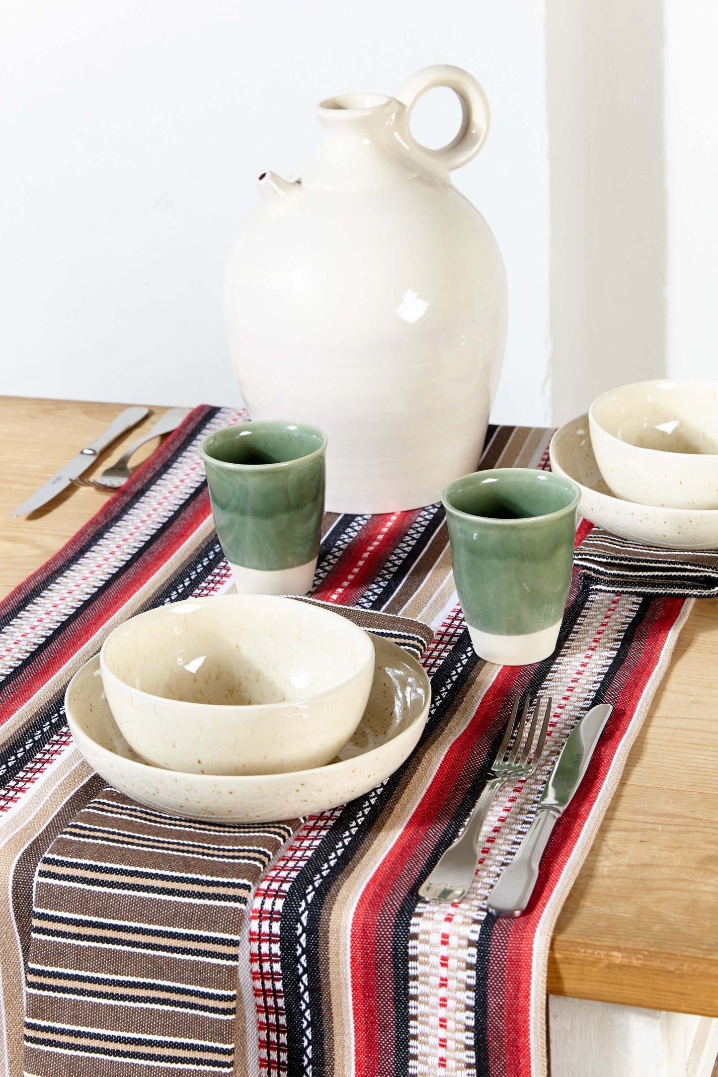 Traditional Spanish woven table runner in red, brown, and white stripes, styled on a wooden table with rustic dishes.