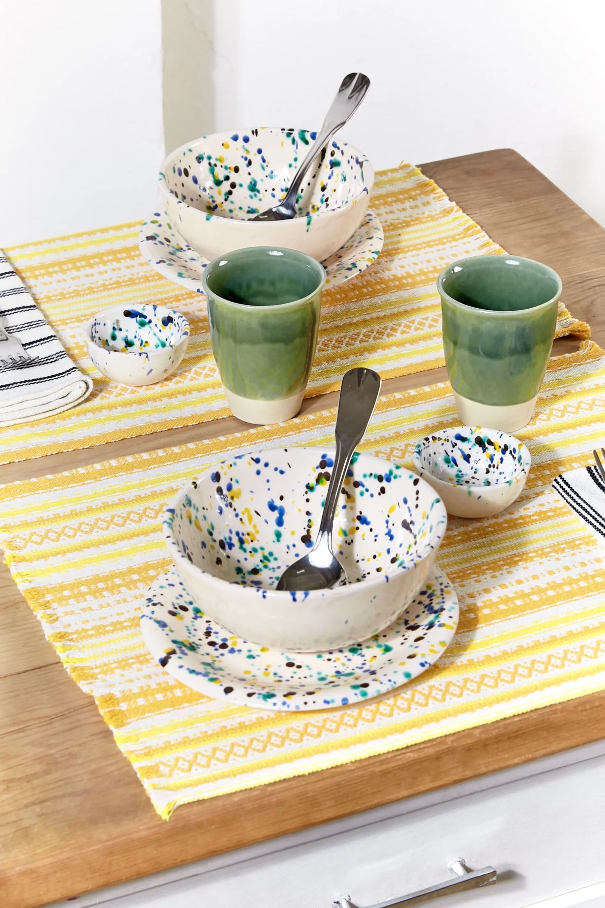Two yellow striped Alpujarra placemats with woven textured fabric on a wooden table, set with artisan ceramics.