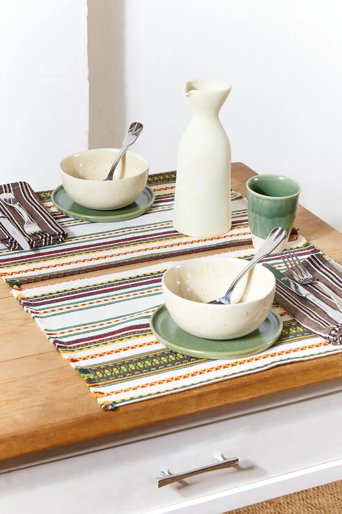 Pack de dos manteles individuales de estilo manchego, tejido crudo con rayas coloridas sobre mesa de madera.