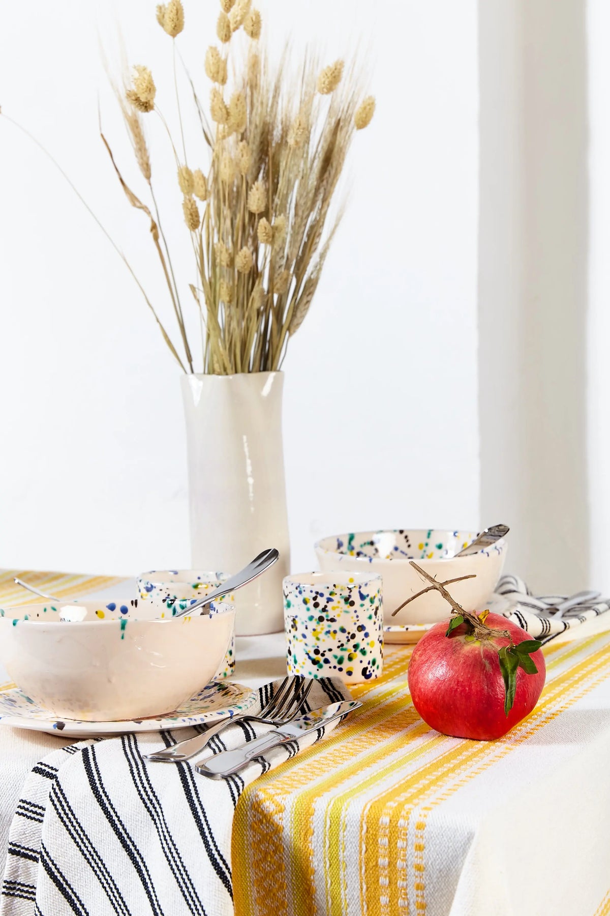 Mantel de estilo alpujarreño con rayas amarillas y blancas, sobre mesa decorada con vajilla artesanal y una granada.