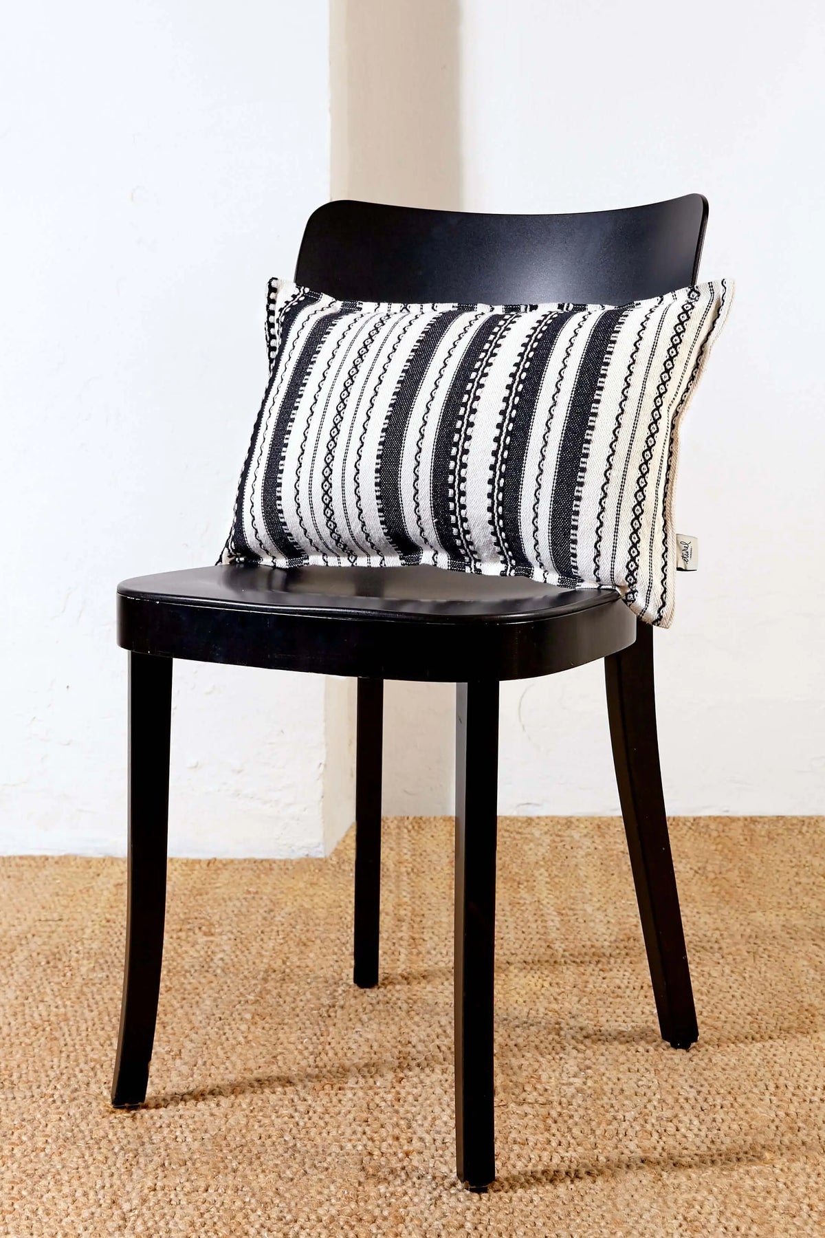 Funda de cojín rectangular 30x50 cm con diseño alpujarra a rayas blancas y negras sobre silla negra de madera.