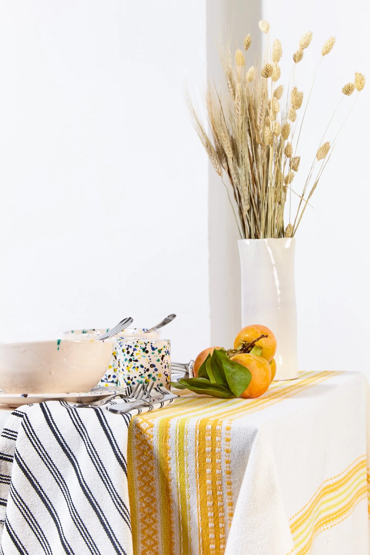 Mantel de tela con rayas horizontales en tonos amarillos y blancos sobre una mesa con vajilla y decoración natural.