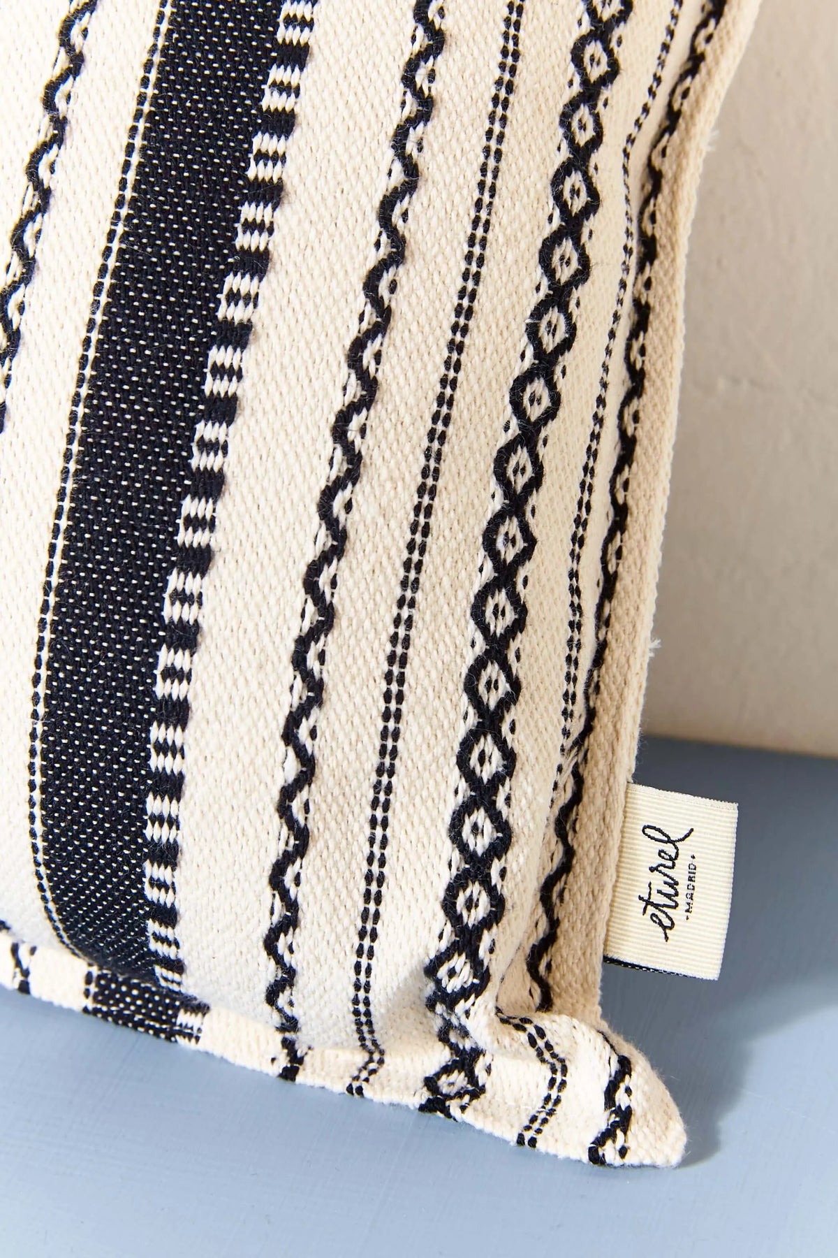 Rectangular cushion cover with a black and white striped Alpujarra-style woven fabric pattern and a fabric brand tag.