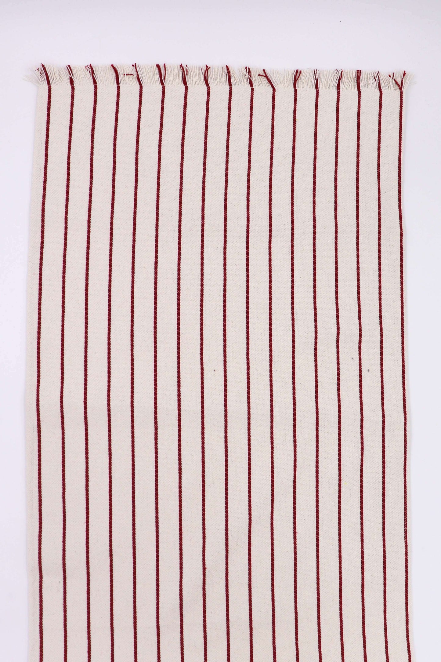 Camino de mesa granate con rayas verticales sobre fondo claro, tejido artesanal con flecos