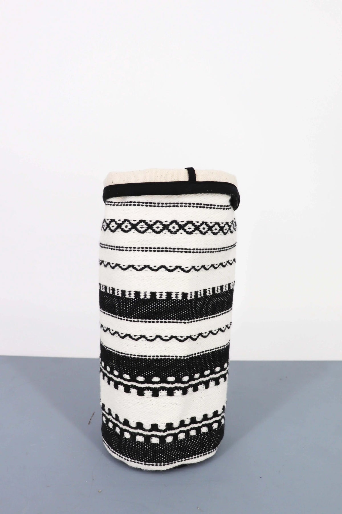 Funda cilíndrica de tela en blanco y negro con patrones geométricos y étnicos tejidos, estilo rústico decorativo.