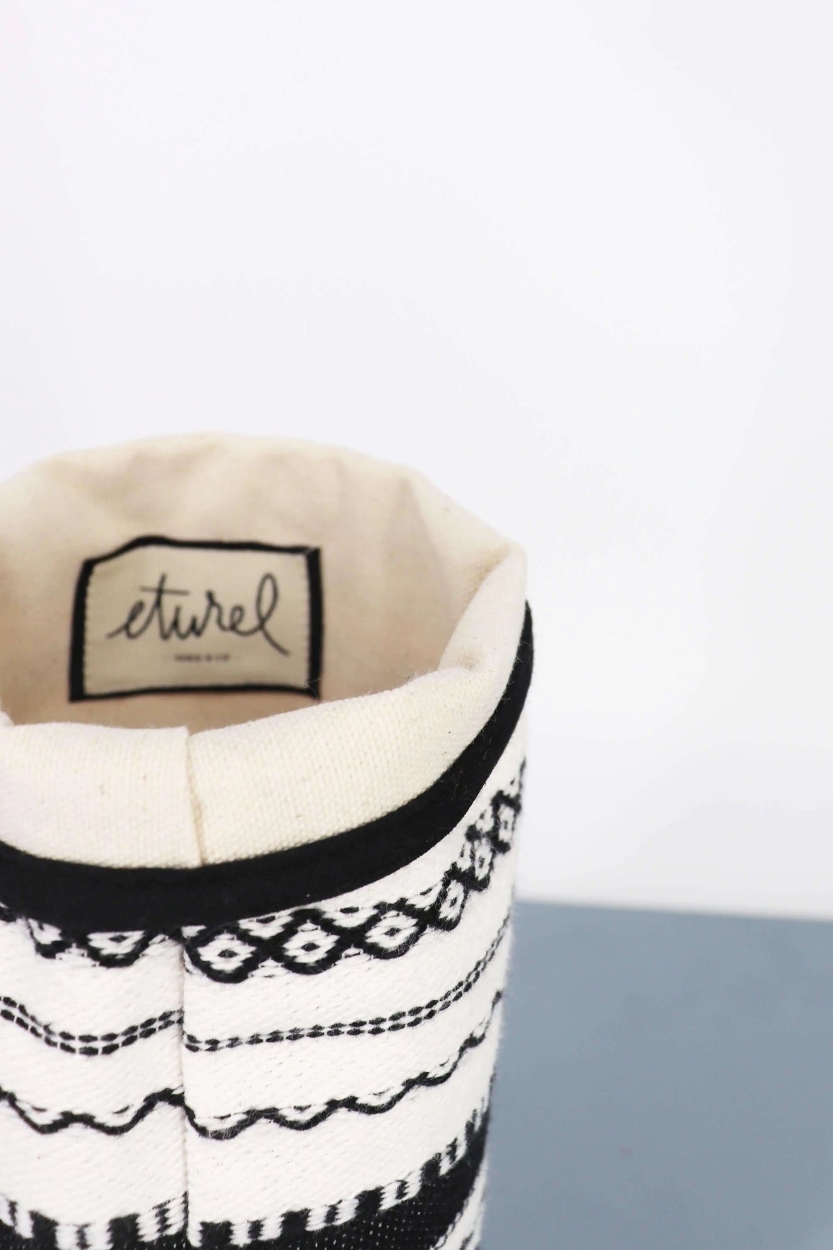 Funda para jarrón de tela de algodón con diseño artesanal de rayas y patrones geométricos en blanco y negro.