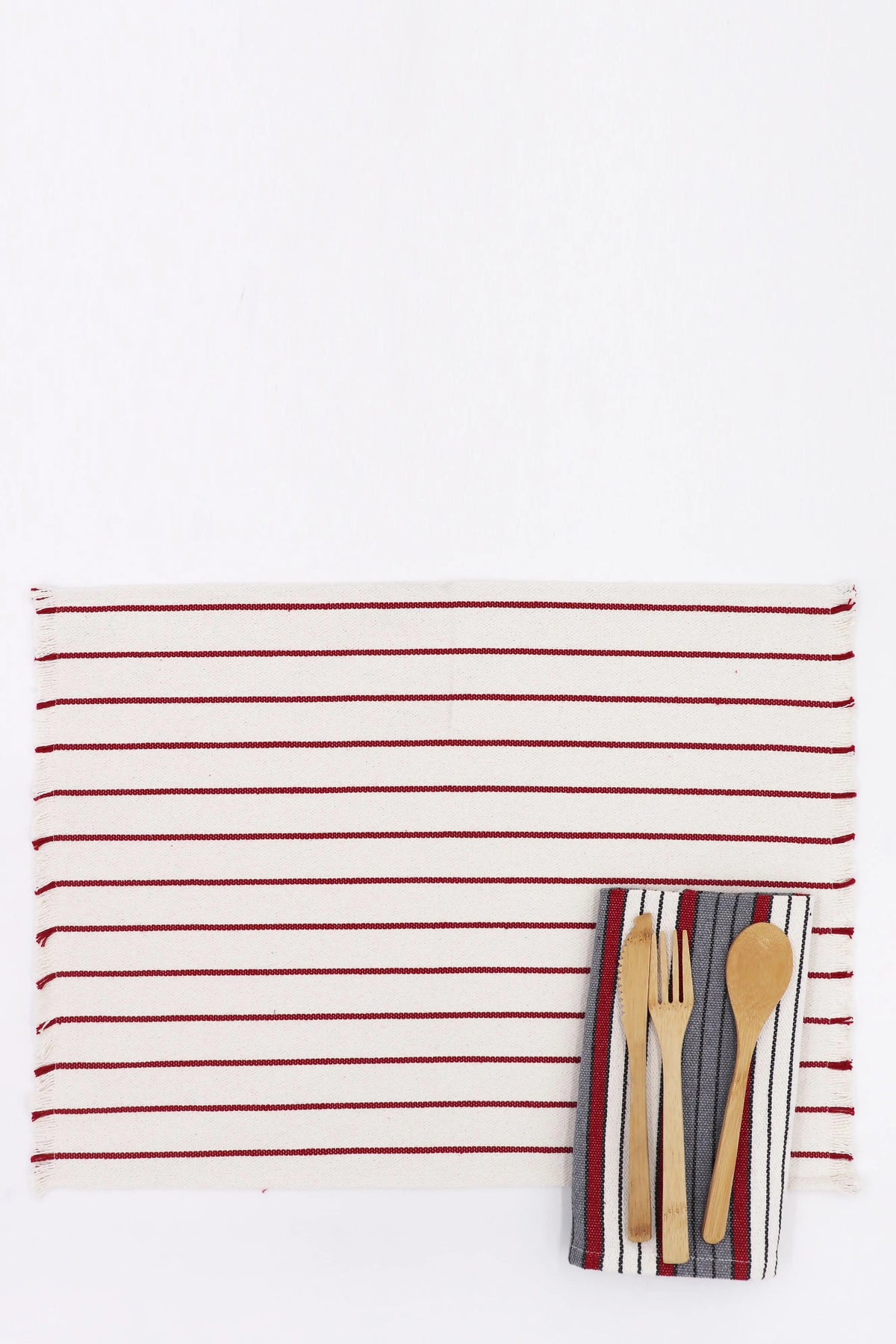 Rectangular cream placemat with thin maroon stripes and frayed edges, topped with a striped napkin and wooden cutlery.