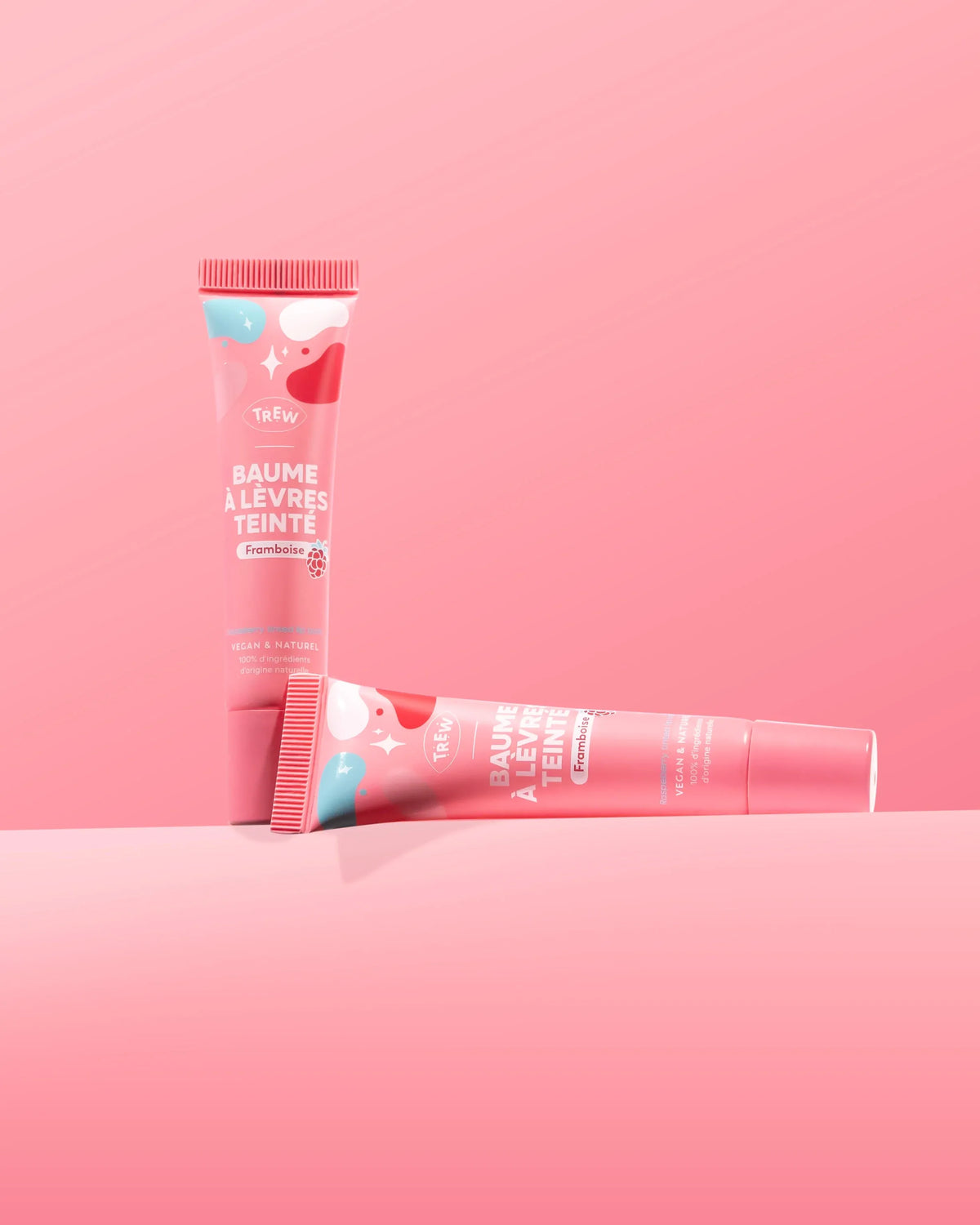 Two pink tubes of raspberry tinted lip balm with white abstract patterns, one standing upright, one lying horizontally.