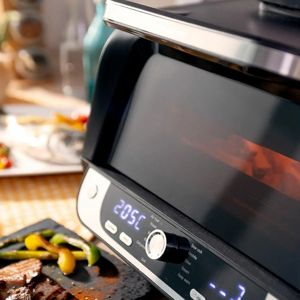 Freidora de aire negra con acabado metálico, panel digital táctil y control giratorio, cocinando alimentos en cocina.