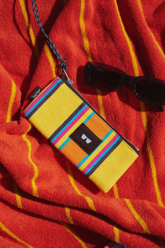 Yellow, orange, and blue striped canvas glasses case with a cord, set against a striped orange beach towel.