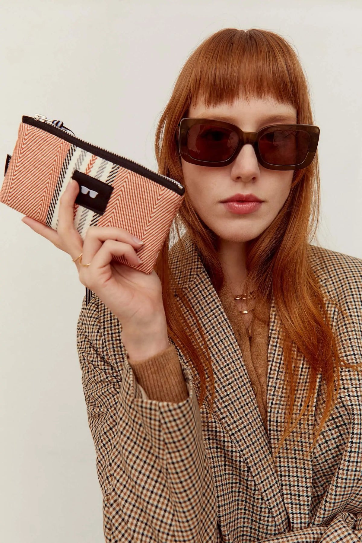 Funda de gafas rectangular con estampado de espiga en tonos arcilla y crema, con cierre de cremallera y etiqueta frontal.