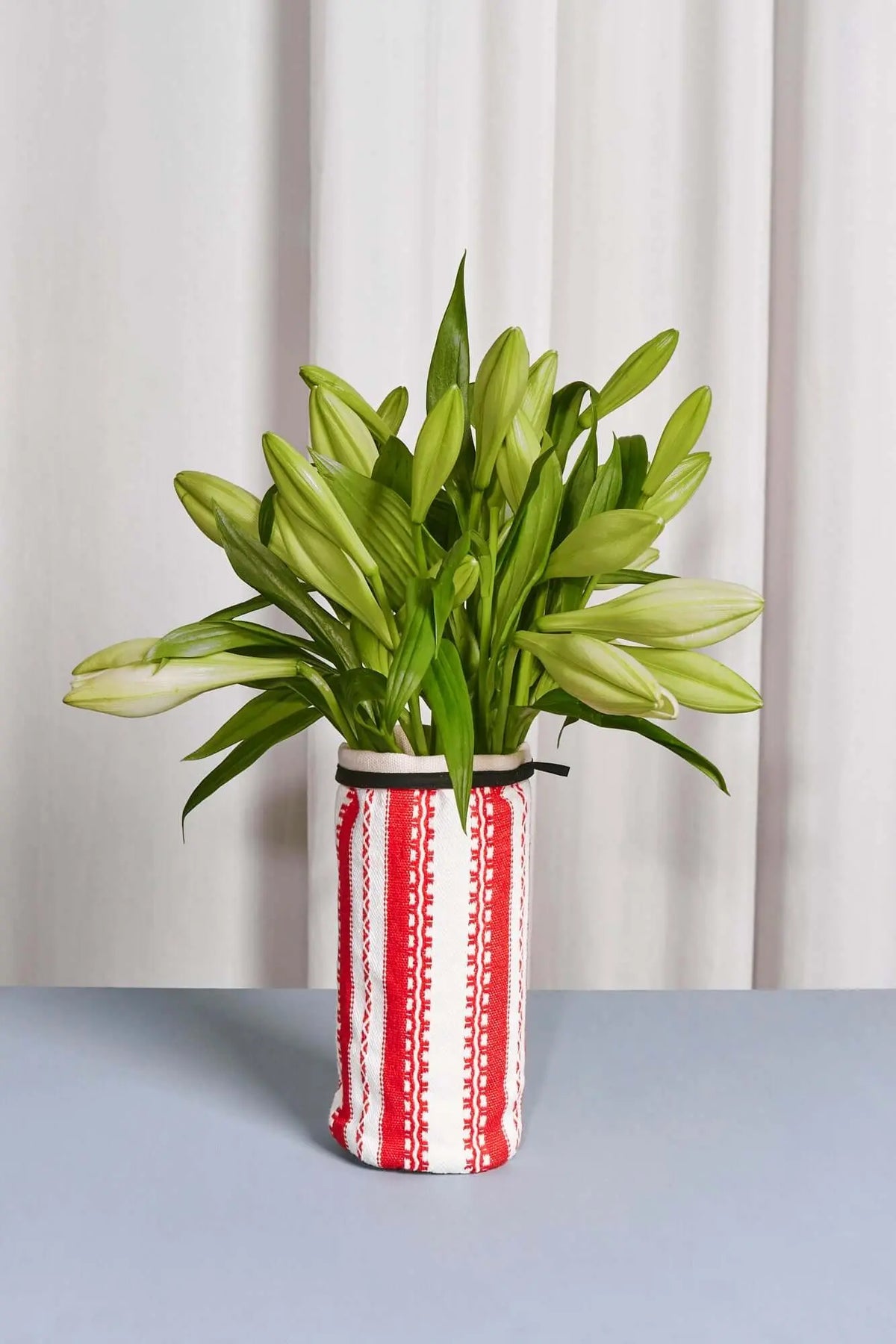 Funda textil cilíndrica con rayas verticales rojas y blancas, detalle en borde superior y flores verdes en el interior.